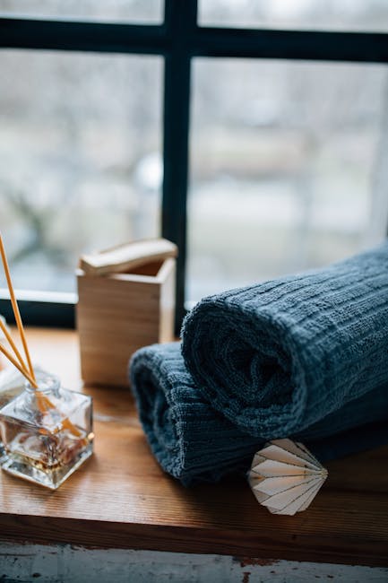 Warm still life featuring rolled towels and a reed diffuser by a window.